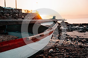 Old abandoned boat with rusted and chipped red and white paint, on a rocky beach at early morning sunrise golden hour