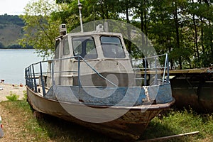 Old abandoned boat, ship on the shore against the background of trees and river