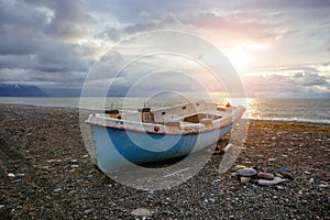 Old abandoned broken fishing boat on sea shore at sunset