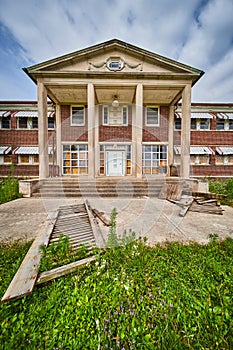 Old abandoned building exterior with stone pillars and brick with overgrown fields