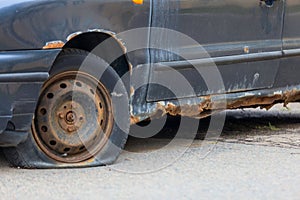 Old abandoned car with a rusting bottom and a flat wheel.