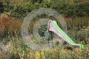 Old abandoned children plastic slide among heavy vegetation