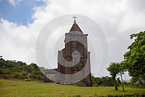 Old abandoned church in green field. Medieval ruin in summer landscape. Christian temple from brown stone.