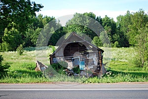 An old abandoned dilapidated village house near the road on a Sunny summer day. Russian provinces.