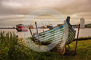 Old abandoned fishing boat with a small one-car ferry in the background and an industrial port