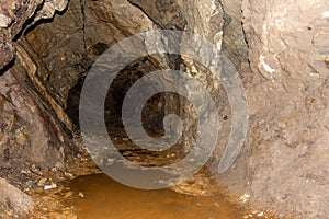 Old abandoned gold mine underground tunnel with rusty water lake. Dangerous tunnel full of dirt and rusty equipment.