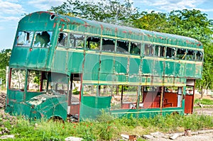 Old abandoned green double decker bus with broken and shattered window glass, damaged and left to rust