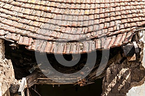 Old abandoned house collapsed roof with damaged vintage tiles after natural disaster of earthquake or hurricane