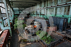 Old abandoned overgrown factory with rusty remains of industrial machinery in workshop