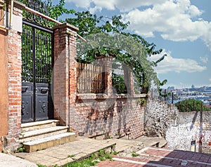 Old abandoned red bricks fence, wrought iron door and green trees on sunny summer day, Balat district, Istanbul, Turkey