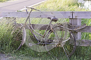 An old abandoned rusty bike parked against a wooden fence