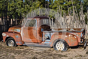 Old abandoned rusty truck in a dry field with a wooden fence