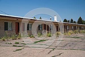 Old, abandoned seedy motorcourt style motel, decays in the sun. Weeds overgrowing in the parking lot