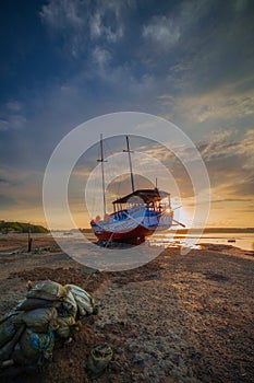 Old abandoned ship on the ocean shore. Broken ship. Sandy beach. Sunset view. Cloudy sky. Sun on horizon. Vertical layout. Copy