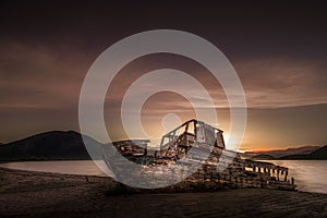 An old abandoned shipwreck, wrecked boat sunken ship stand on beach coast. Scenic sunset sky. Old Fishing Boat Wreck