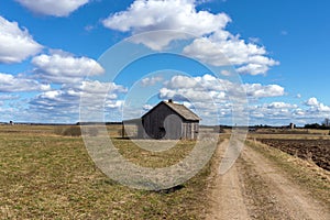 An old abandoned small wooden house in the field blue sky white clouds, barn or scary concept