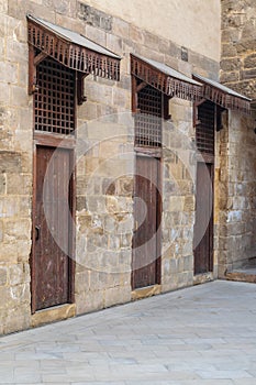 Old abandoned stone bricks wall with three weathered wooden doors covered with wooden grid