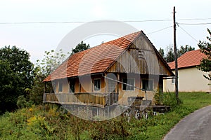 Old abandoned stone and wooden family house with front porch surrounded with overgrown forest vegetation next to tall wooden