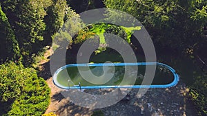 Old abandoned swimming pool with dirty green water. Flight over a beautiful green area with an abandoned pool.