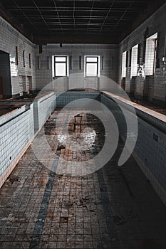 An old abandoned swimming pool. Wooden chair at the bottom. Dirty floor. Shabby walls. Blue tiles.