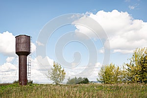 An old abandoned water tower stands in the middle of a green meadow on a summer elephant day. A rusty metal water tower fortified