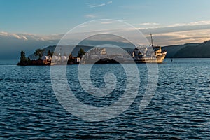 Old abandoned white ships on small island with trees in blue sea in the light of the setting sun against the backdrop of mountains