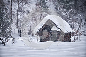 Old abandoned wooden house. The roof is covered with a thick layer of snow. Altai in winter season