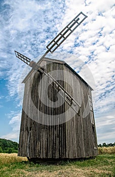 Old abandoned wooden mill and wheat summer field