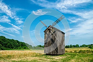 Old abandoned wooden mill and wheat summer field