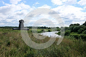 Old abandoned wooden windmill in the field by the river