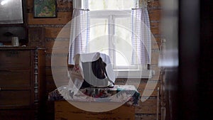 An old accordion in Russian style stands on the windowsill in a wooden ancient house covered with a white embroidered