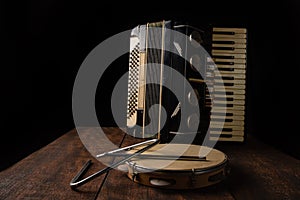 Old accordion, tambourine and triangle on rustic wooden surface with black background and Low key lighting, selective focus photo