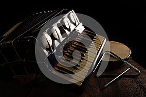 Old accordion, tambourine and triangle on rustic wooden surface with black background and Low key lighting, selective focus photo