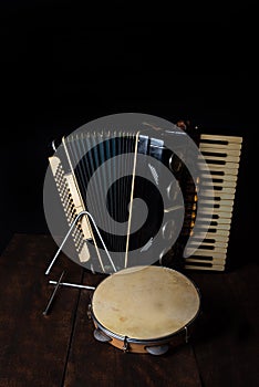 Old accordion, tambourine and triangle on rustic wooden surface with black background and Low key lighting, selective focus photo