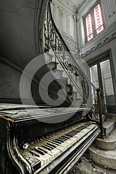 An old ad weathered grand piano in front of a spiral staircase