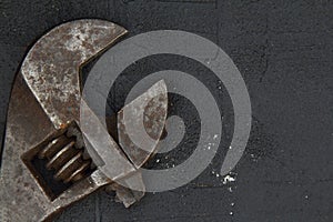 Old adjustable wrench on rusty metal sheet. Sliding forged wrench against a dark industrial background