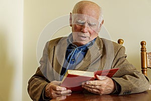 Old age, leisure and people concept - senior man sitting on sofa and reading book at home. Slavic appearance. Elderly