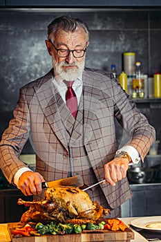 Old-aged handsome man in formal expensive suit cutting out roasted chicken