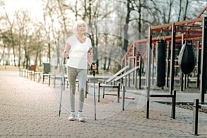 Old-aged laughing woman doing Nordic walking on the sportsground