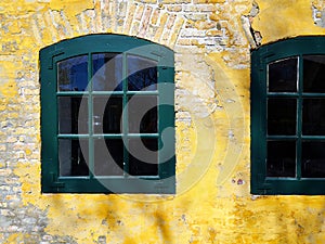 Old aged wooden window with cracked paint on a yellow painted wall