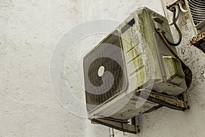 An old and aging Split type air conditioner condenser mounted on the exterior wall. Grimy and covered in slight moss and rust.