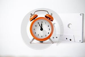 Old analog orange clock on a white background. The clock shows the time from five minutes to twelve o`clock, and next to it is a