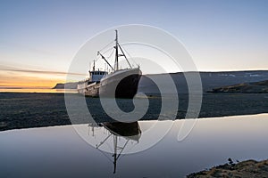 Old ancient, destroyed and abandoned norwegian whaling ship laying ashore in the westfjords of Iceland during sunset.