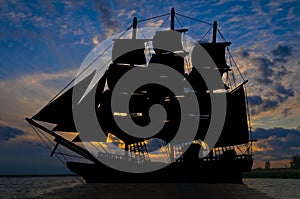 Old ancient pirate ship silhouette on peaceful ocean at sunset background