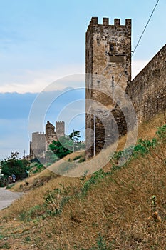 Old ancient stone wall and towers of Genoese fortress in Sudak made of sand brown colored bricks stand on steep slope with dry yel