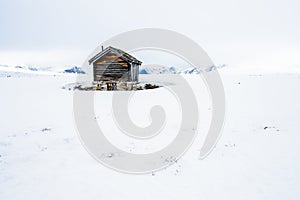 A old and ancient wooden cabin outdoors in beautiful snow covered mountains and foggy scenery with cross coutry skiiers
