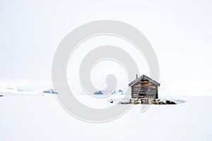 A old and ancient wooden cabin outdoors in beautiful snow covered mountains and foggy scenery with cross coutry skiiers