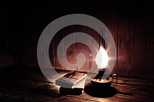 Old antique books with burning paraffin lamp near on the wooden table.