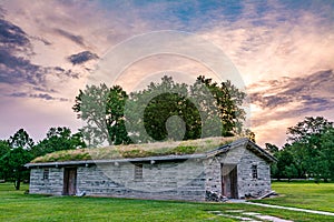 Old antique building in Nebraska with a sod roof surrounded by t