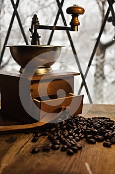 Old antique coffee grinder with coffee beans on a wooden windowsill.